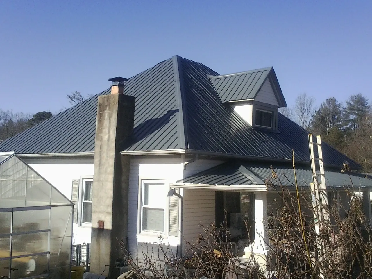Dark blue standing seam metal roof on a white farmhouse with dormer — Slate & Tile Roof Repair by Roofing Brothers in Bertram