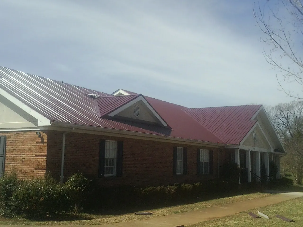Red metal roof with gabled entries on a long brick building, from a Hail Damage Roof Repair job in Bertram