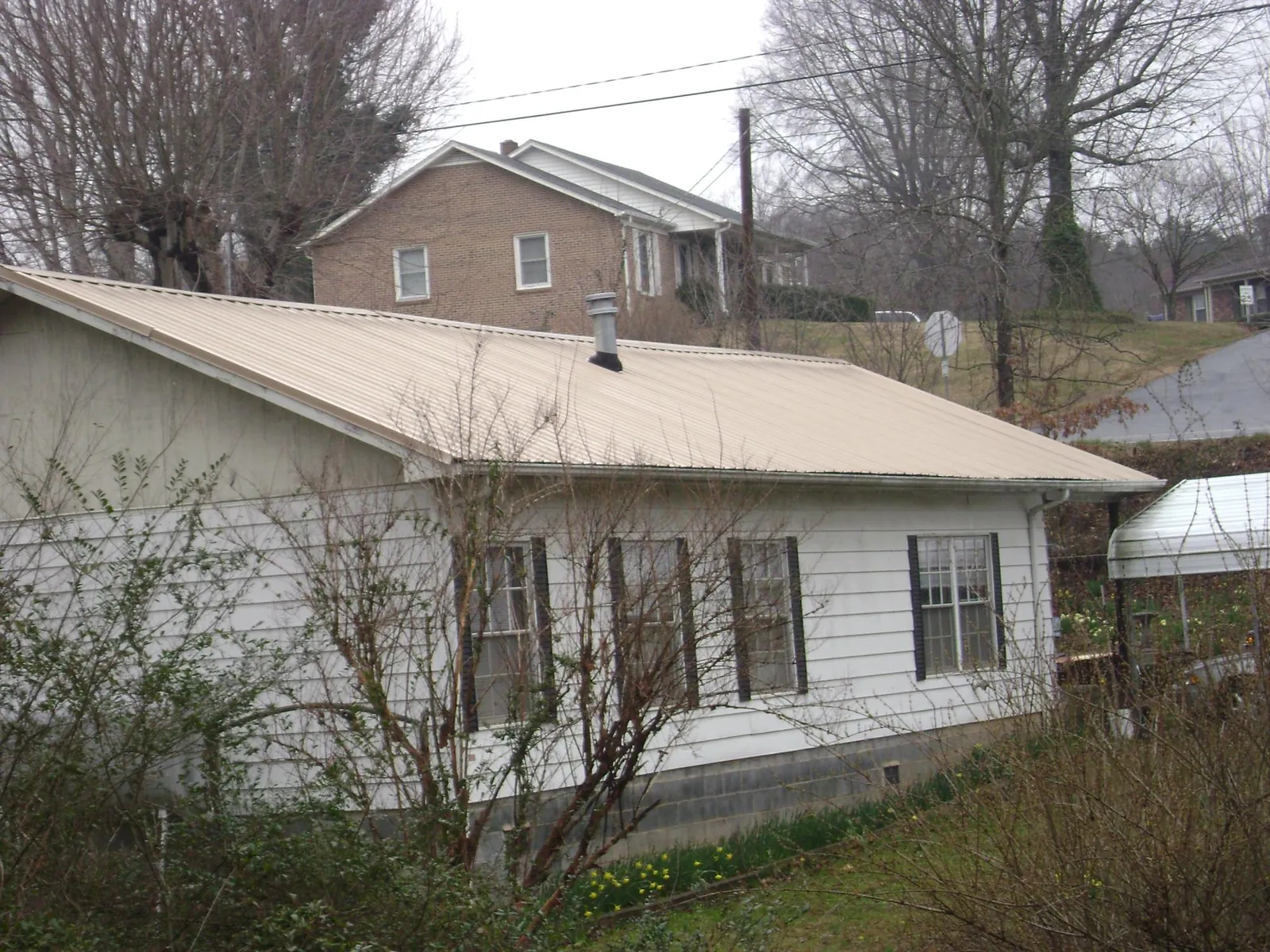 Tan metal roof on a white sided house set into a hillside — Commercial Roofing by Roofing Brothers in Bertram
